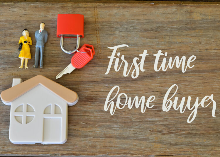 Toy house, keys, padlock and people miniatures over wooden background written with FIRST TIME HOME BUYER